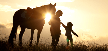 Mother and daughter with horse standing in a field at sunset.