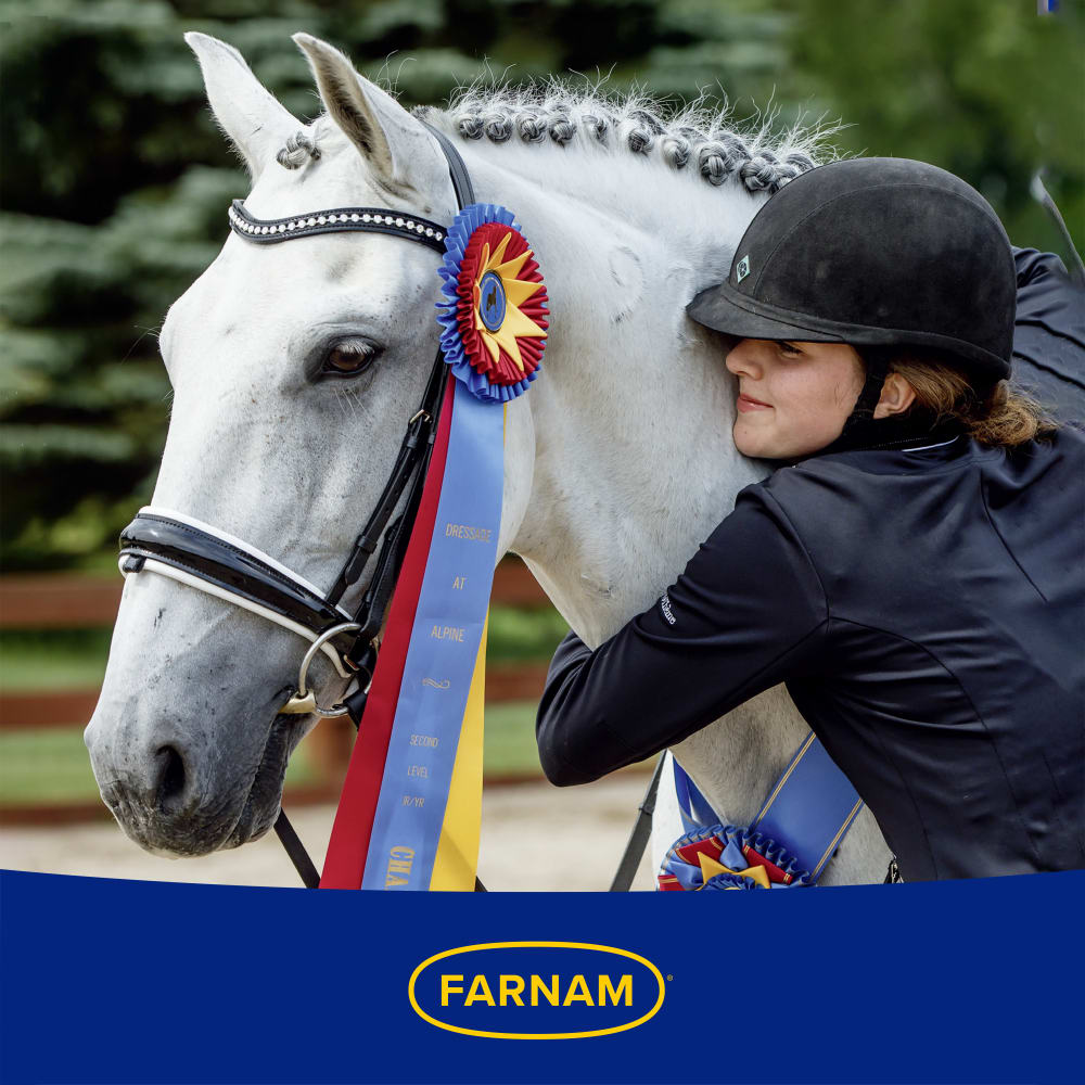 Young woman in jockey uniform hugging white horse with a prize ribbon. Farnam logo