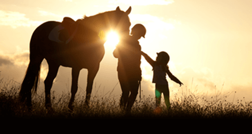 Mother and daughter with horse standing in a field at sunset.